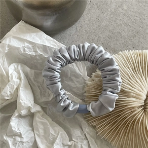 Detailed view of grey satin scrunchie with pleated texture and blue oval decorative buckle