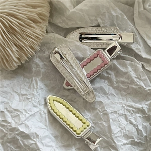 Détail de pinces à cheveux géométriques argentées, roses et jaunes à bords ondulés