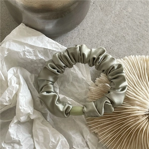 Close-up of sage green satin scrunchie with olive button on minimalist textured background