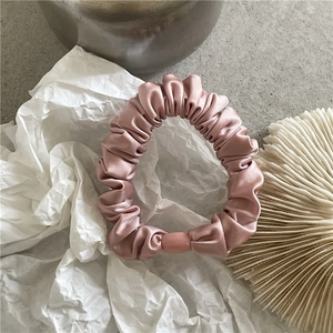 Detail of a dusty pink satin scrunchie with soft sheen and decorative translucent beads