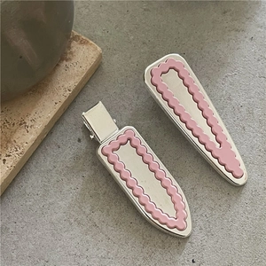 Détail de pinces à cheveux argentées avec bordures roses ondulées sur fond de pierre