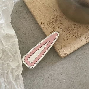 Détail d'une pince à cheveux rose à bords festonnés et base métallique sur un plateau