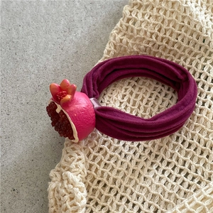 Detailed shot of purple fabric hair tie with realistic pomegranate charm on mesh bag