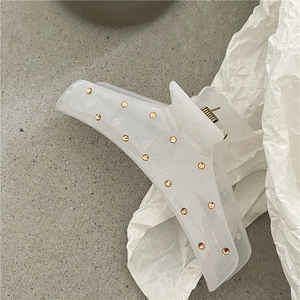 Dettaglio molletta capelli bianco crema traslucido con borchie dorate su pietra