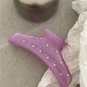 Dettaglio molletta per capelli viola traslucida con strass rosa su superficie in pietra