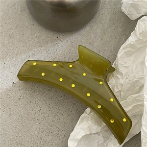 Dettaglio di un fermaglio per capelli verde oliva con strass gialli su un pavimento grigio