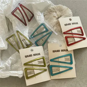 Dettaglio di fermagli triangolari in metallo rosso, blu e verde su carta fatta a mano