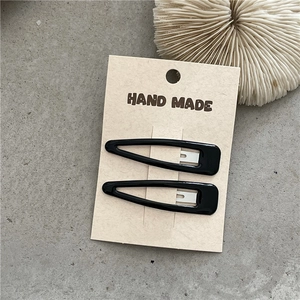Detail of 2-pack black teardrop BB hair clips on minimalist beige card packaging