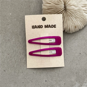 Detail view of two rose red teardrop hair clips on a handmade card display
