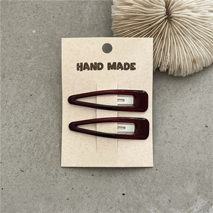 Detail of dark red resin triangular hair clips on a Hand Made branded paper card