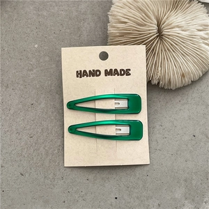 Detail view of two green teardrop hair clips on beige card with handmade text