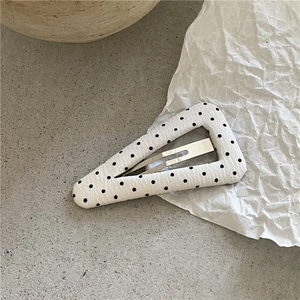 Détail d'une pince à cheveux triangulaire en tissu blanc à pois noirs sur fond de pierre