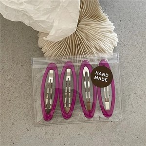 Detail view of 4 purple translucent geometric hair clips in handmade packaging on stone background