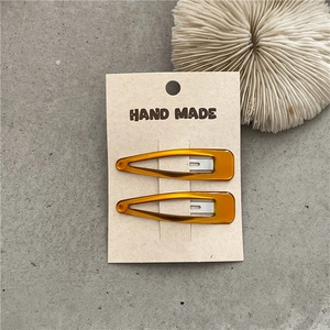 Detail view of two amber resin water-drop hair clips on a handmade branded display card