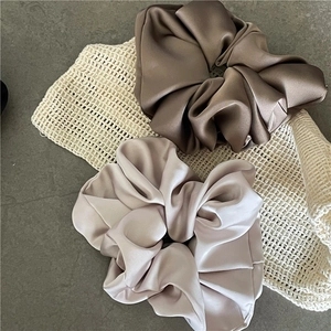 Detailstruktur der braunen und champagnerfarbenen Satin-Scrunchies auf Steinplatte