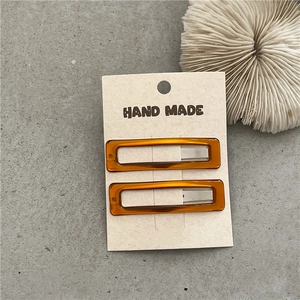 Detail view of two rectangular amber resin hair clips on display card with white coral decor