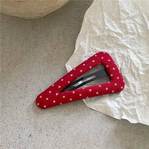 Détail d'une pince à cheveux rouge à pois blancs en tissu avec fermeture à clip en métal