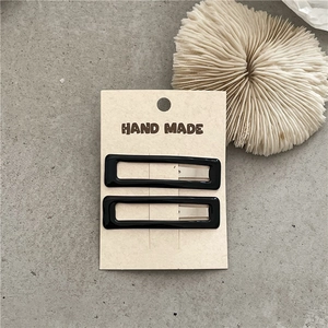 Close-up of two black rectangular minimalist hair clips on a white handmade display card