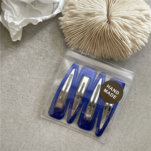 Detail view of four blue drip oil hair clips in handmade packaging on textured background