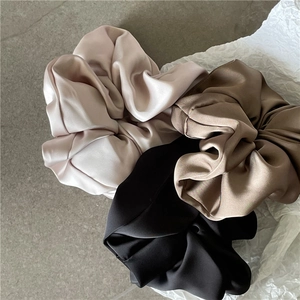 Detaillierte Nahaufnahme von drei Satin-Haargummis in Champagner, Kaffee und Schwarz Seidenoptik