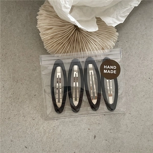 Detailed view of four handmade colorful geometric oval hair clips in a branded package