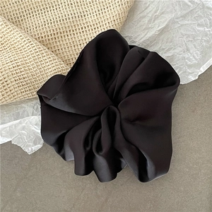 Nahaufnahme des schwarzen Satin-Haargummis mit weicher Seidentextur und elegantem Faltenwurf