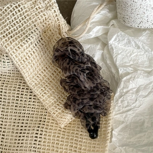 Dettaglio del fermaglio a banana in rete leopardata con tessuto in chiffon plissettato su sfondo
