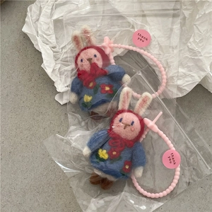 Close-up of handmade wool felt rabbit dolls in red hoods and gift packaging with pink beads