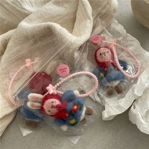 Detailed view of handmade felt bunny charms in floral dresses with cute packaging