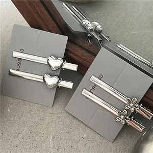 Minimalistische zilveren metalen haarspelden met 3D-hart en bloemaccent op grijze kaart