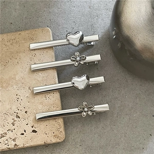 Detail van vier zilveren metalen haarclips met hart en bloem op een stenen ondergrond