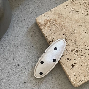 Détail d'une barrette BB ovale en tissu de soie crème avec des motifs à pois noirs