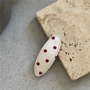 Détail d'une pince à cheveux ovale en tissu crème à pois rouges posée sur une pierre naturelle