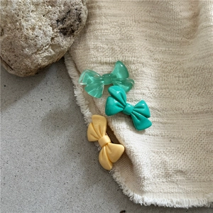 Detailed macro view of resin bow hair clips in pastel mint and yellow on linen