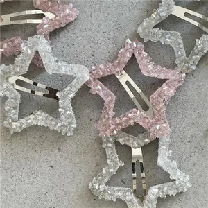 Dettaglio di fermagli per capelli a stella con cristalli rosa e bianchi su superficie grigia