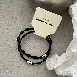 Detail of two black elastic hair ties with gold beads on minimalist paper card packaging
