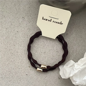 Detail view of two dark brown elastic hair ties with gold metal beads on a handmade card