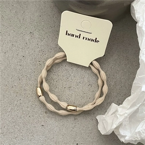 Close-up of beige hair ties with wavy texture and gold metal accents on a card