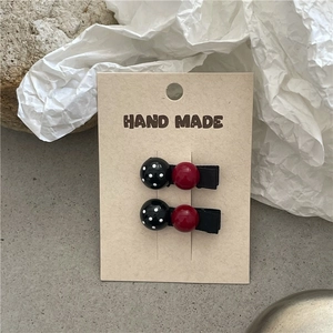 Detailed view of handmade polka dot hair clips with red beads on a display card