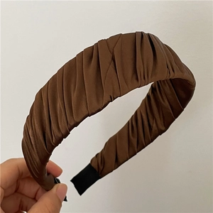 Détail d'un serre-tête plissé en satin café foncé avec une texture de tissu lisse et embouts