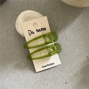 Macro shot of two translucent green waterdrop-shaped hair clips on a beige card holder