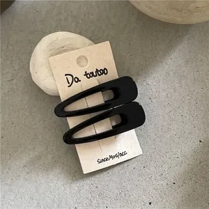 Close-up of two glossy black water-drop hair clips on a minimalist display card