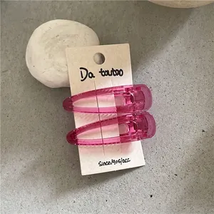 Detail of two translucent rose pink water drop hair clips on a beige display card