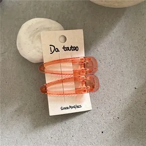 Detail view of orange translucent teardrop hair clips on beige display card texture