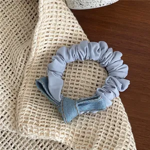 Detailed view of light blue denim bow scrunchie with yellow stitching on beige knit