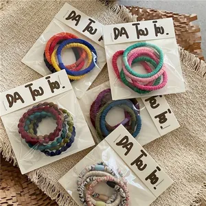 Five-pack of cream colored elastic scrunchies with ripple texture and colorful beads