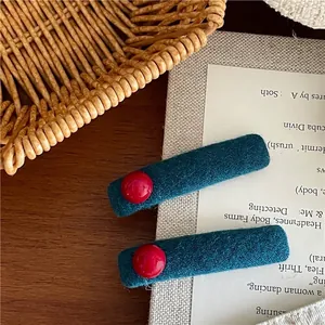 Paar Vintage-Haarklammern aus blaugrünem Filz mit roten Perlen auf Holztisch
