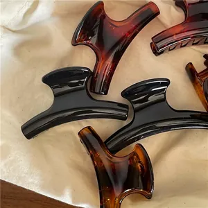 Glossy black and tortoise shell resin hair claws on neutral linen fabric background