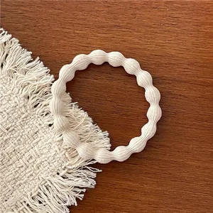 Detailed view of beige elastic hair tie with pearl-like wavy texture on a wooden surface