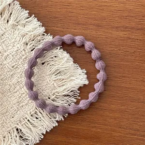Detail showing the purple textured bubble hair tie on a white woven mat and wood surface